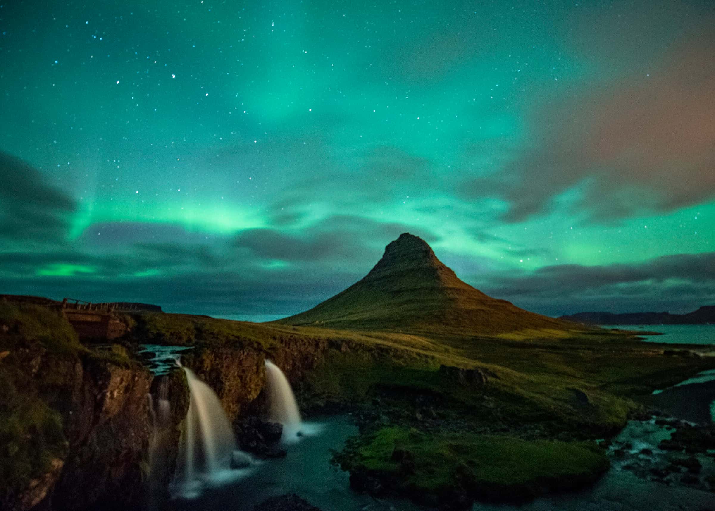 Green aurora borealis arcing over Kirkjufell mountain and its waterfalls at night